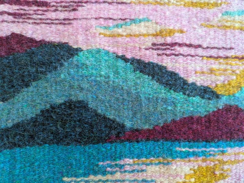 close up of a wool tapestry weaving showing mountains and sky