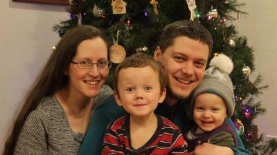 Jacqueline, Randy, and kids smiling in front of a Christmas tree