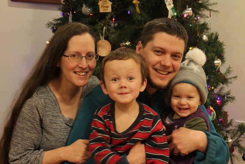 Jacqueline, Randy, and kids smiling in front of a Christmas tree