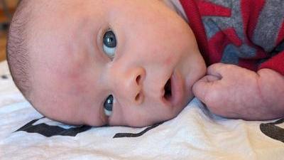 a cute baby lying on his stomach looking out, mouth slightly open as if confused or curious, wearing a red and grey stripy outfit