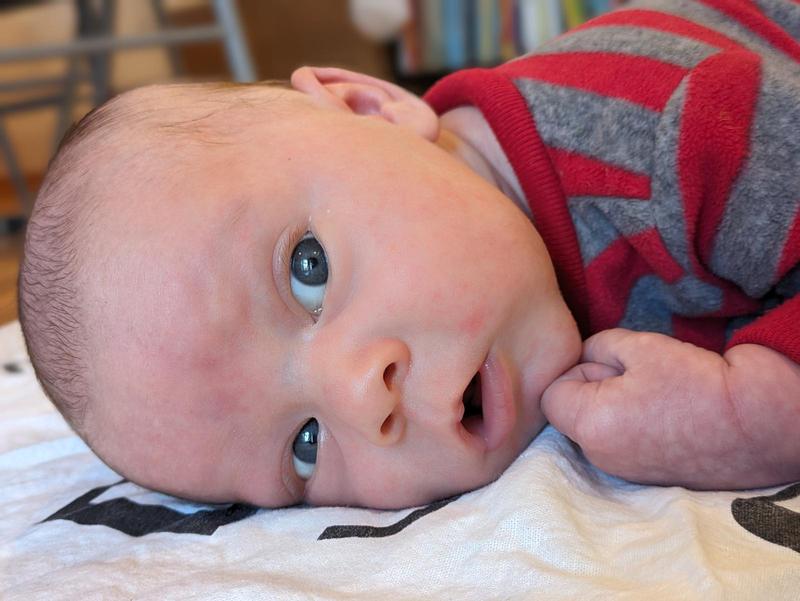 a cute baby lying on his stomach looking out, mouth slightly open as if confused or curious, wearing a red and grey stripy outfit