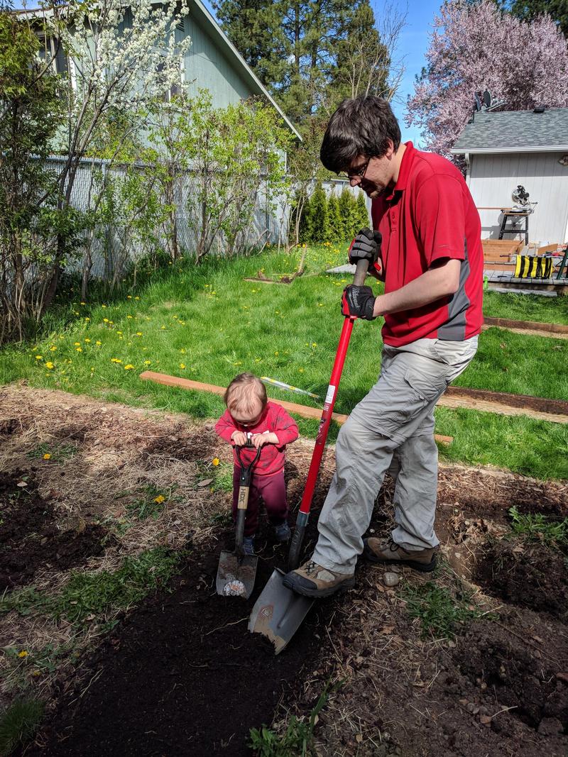 Randy with a big shovel standing next to our 2-year-old with a small shovel, moving dirt in the backyard