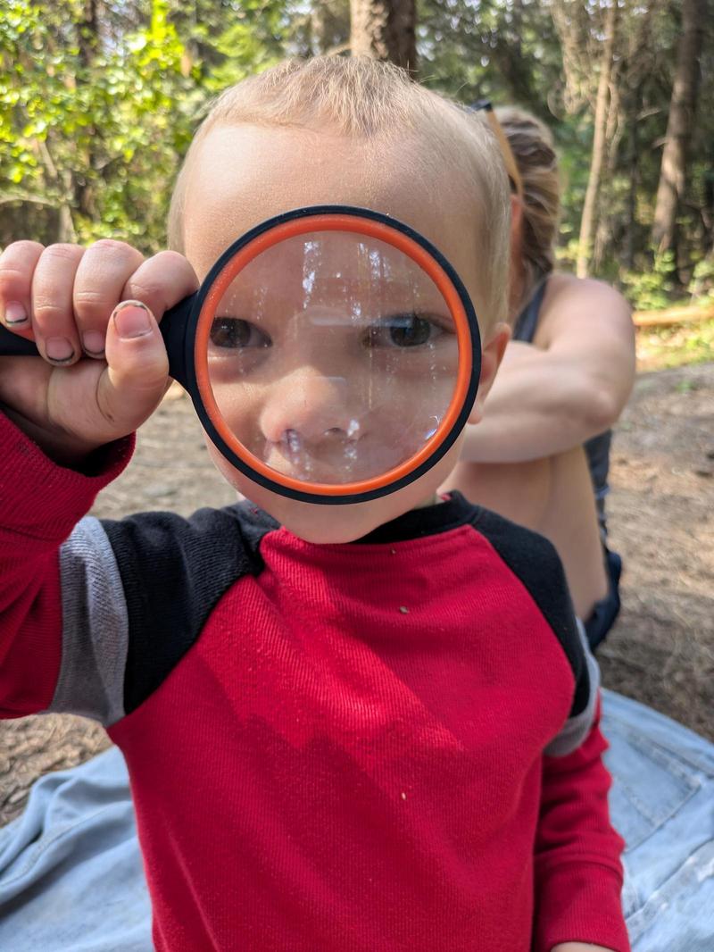 a child in a red shirt holds up a magnifying glass in front of his face, so his eyes and nose look really big