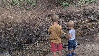 two boys, one big and one small, standing by a creek