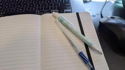 pens on a small notebook in front of a computer and mouse
