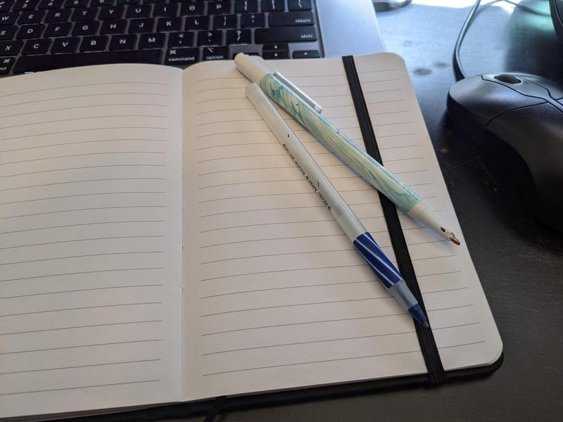 pens on a small notebook in front of a computer and mouse
