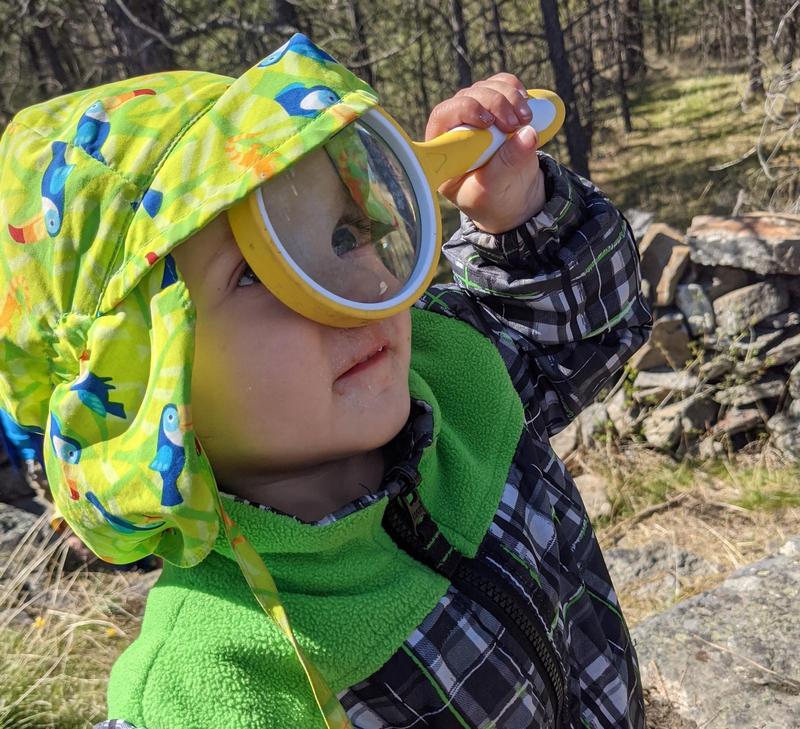 toddler holding a magnifying glass up to her eye and looking up at the sky