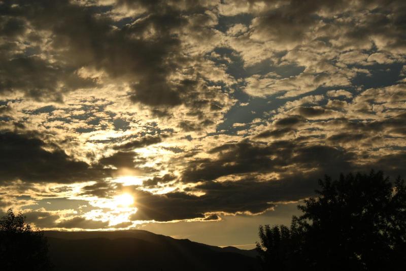 sun setting behind clouds hills silhouetted