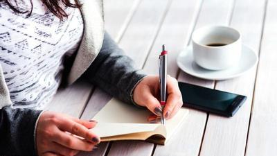woman sitting at a table writing in a small journal with a cup of coffee