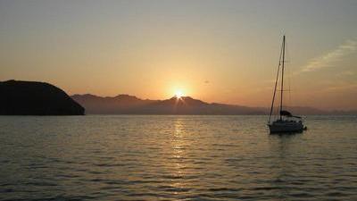 sunrise over the water in La Paz, Mexico with a quiet sailboat in the foreground