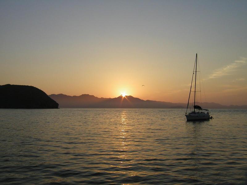 sunrise over the water in La Paz, Mexico with a quiet sailboat in the foreground
