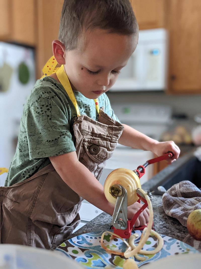 boy standing at a counter spinning apples on an apple peeler-corer-slicer