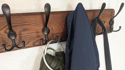 black coat hooks on a wood board on a wall, with a couple coats and bags hanging on them