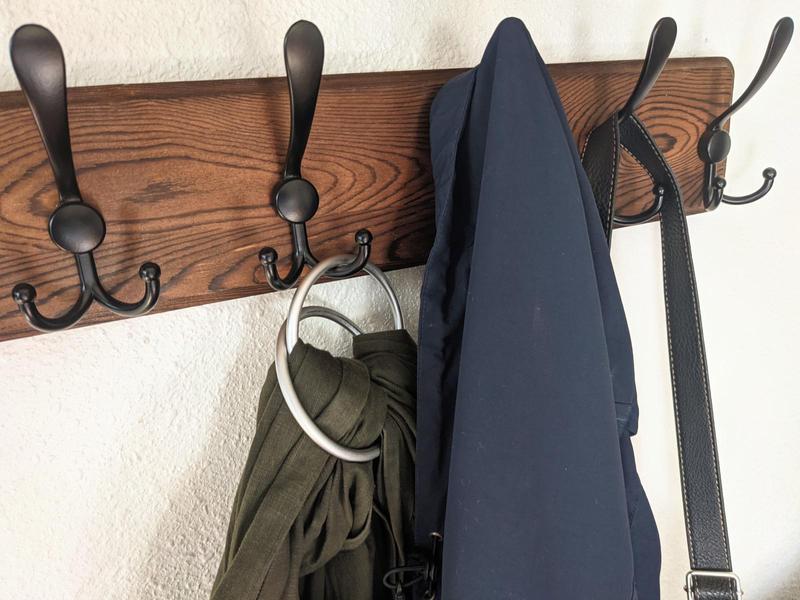 black coat hooks on a wood board on a wall, with a couple coats and bags hanging on them