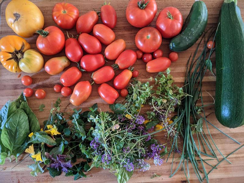 tomatoes, zucchini, cucumber, chives, and a pile of mixed herbs and flowers on a wood cutting board