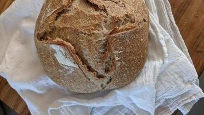 a loaf of warm crusty sourdough resting on a flour sack towel