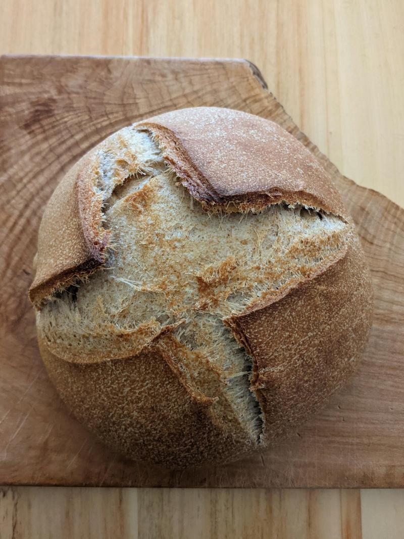 a round loaf of brown sourdough on a wooden cutting board