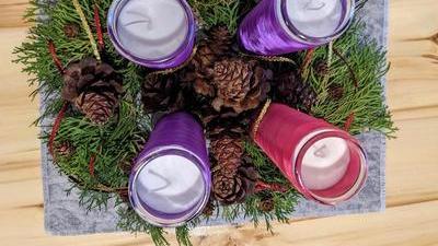 top down view of evergreen advent wreath with four tall ribbon-wrapped candles, one pink and three purple