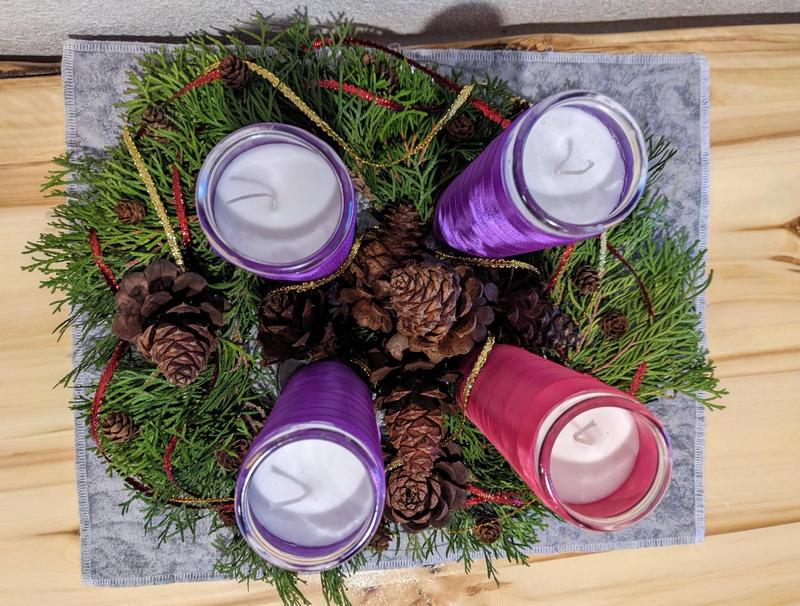top down view of evergreen advent wreath with four tall ribbon-wrapped candles, one pink and three purple