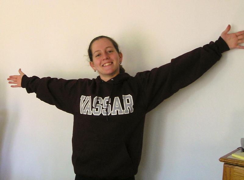 Jacqueline in a Vassar sweatshirt, grinning with arms outstretched