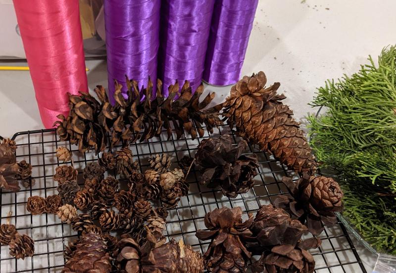pinecones on a cooling rack beside some evergreen branches and ribbon-wrapped tall candles