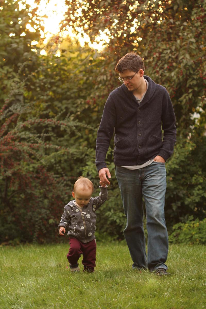 Randy holding his two-year-old son's hand while they walk in the grass