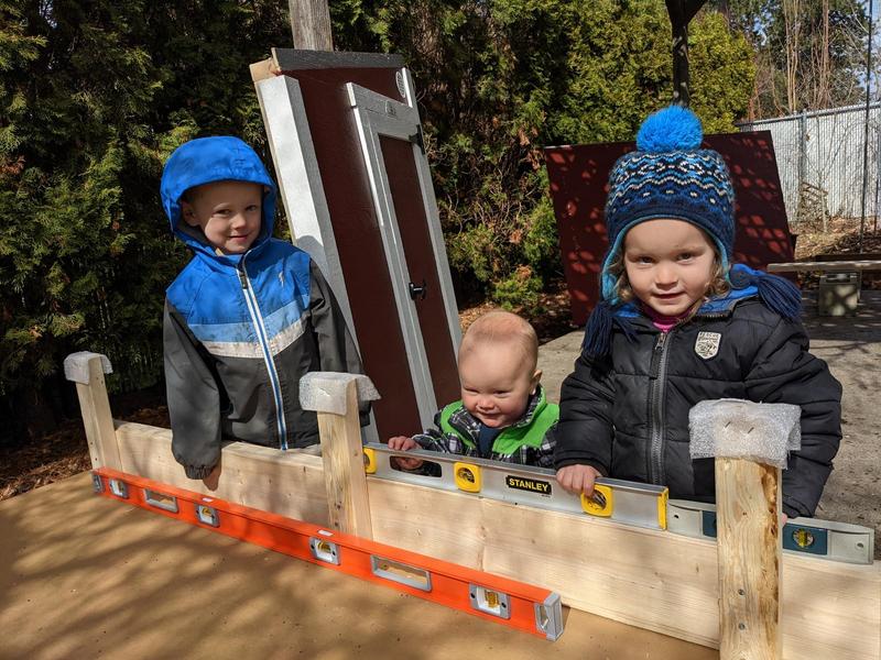 three young kids stand by parts of a disassembled chicken coop, holding levels