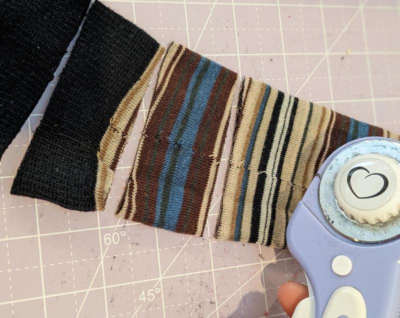 a tall sock laid flat on a rotary cutting mat, being cut into strips