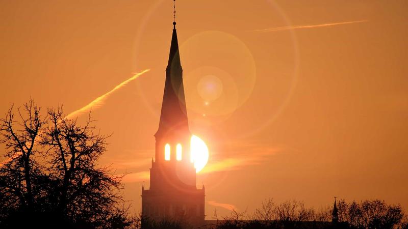 the sun rises behind the steeple of a church