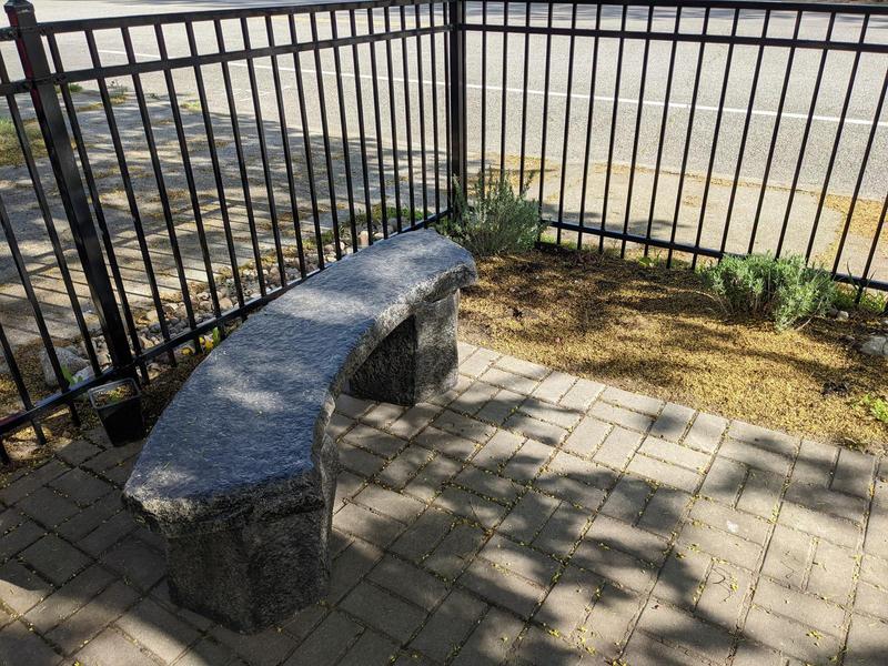 a curved stone bench beside a four-foot high metal fence in our front yard