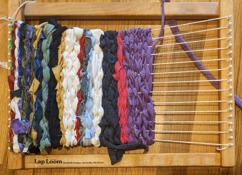 close up of a striped tapestry being woven on a small lap loom with fabric scraps as the weft