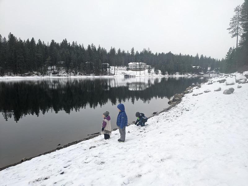 three small kids on a snowy bank of a glassy river