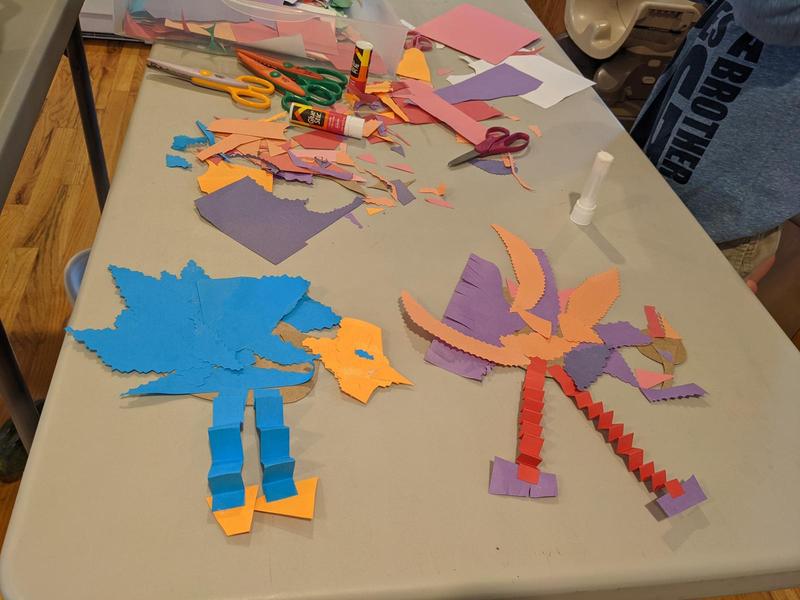 two turkeys made from pieces of colored construction paper and glued together, that don't look much like turkeys, with accordion-folded strips for legs