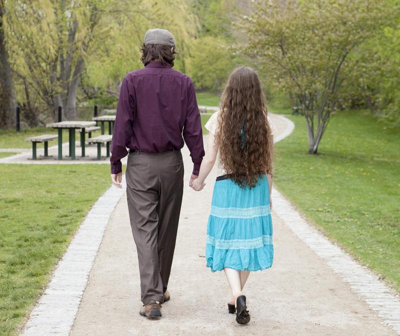 randy and jacqueline walking away on a path in a park toward trees and grass