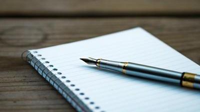 a fancy pen resting on a lined spiral bound notebook