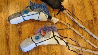 Three homemade sock hobby horses lined up on the floor, made with bright colors and fabrics that aren't particularly horselike