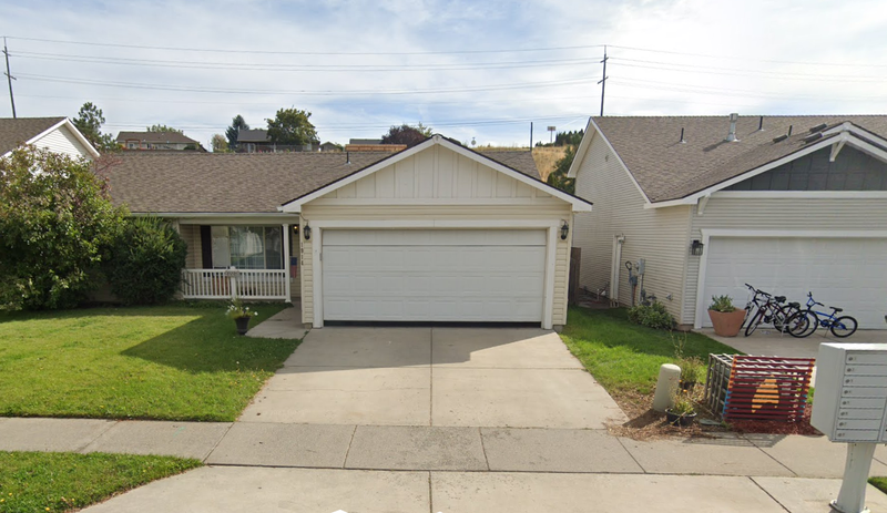 suburban snout-nosed house with a driveway lined by flat lawn, with more grass in the ditch between sidewalk and street; the front door is hidden to the left of the garage