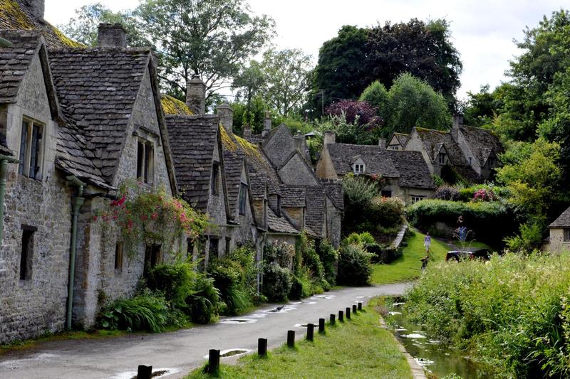 a row of stone cottages along an alley, lined with bushes, shrubs, and greenery