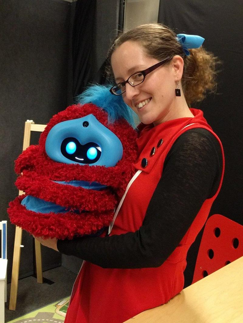 jacqueline in a red dress holding a red and blue striped robot and smiling