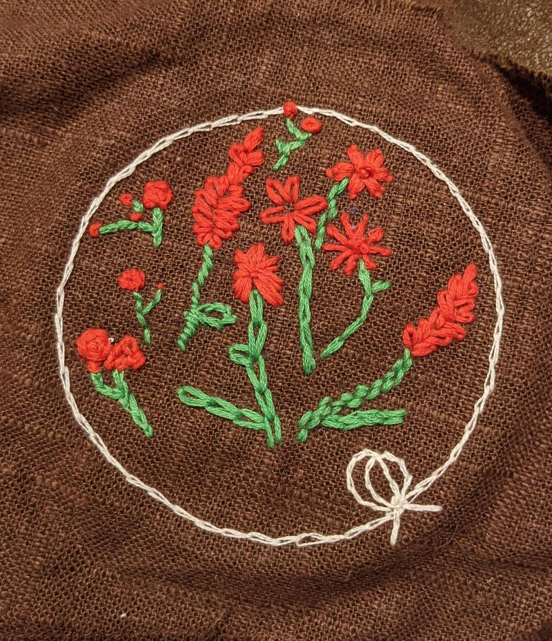 little red embroidered flowers on a square of linen, with an embroidered circle going around them