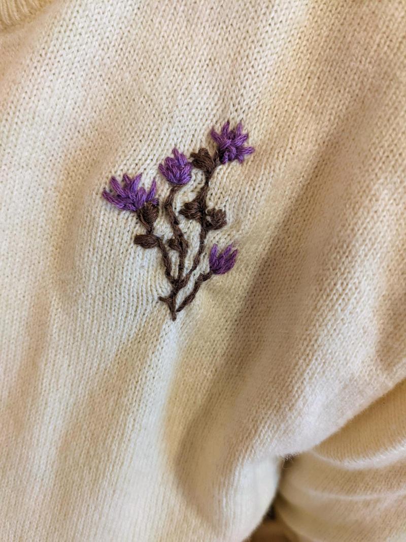 small purple flowers embroidered on a light sweater