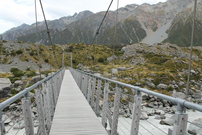 a bridge across a rocky creek in New Zealand with mountains in the background