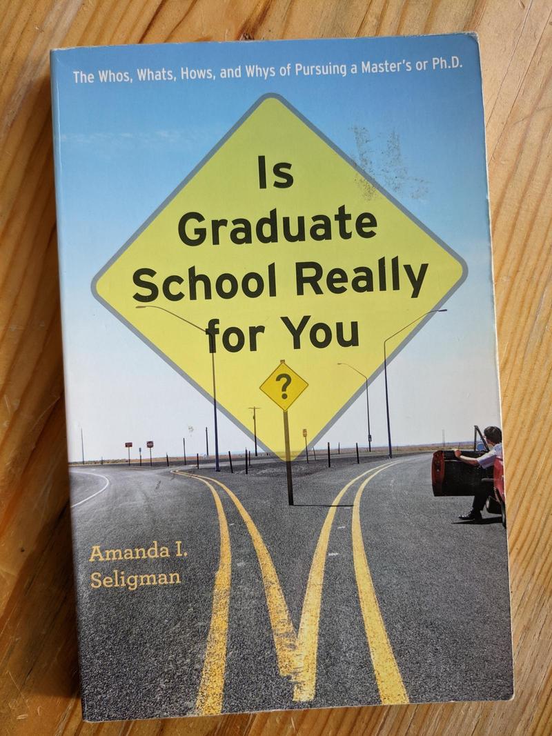 the cover of the book Is Graduate School Really for You? by Amanda I. Seligman, featuring a road splitting left and right with the title in a big yellow street sign above, and a person looking out of a stopped red car on the right road