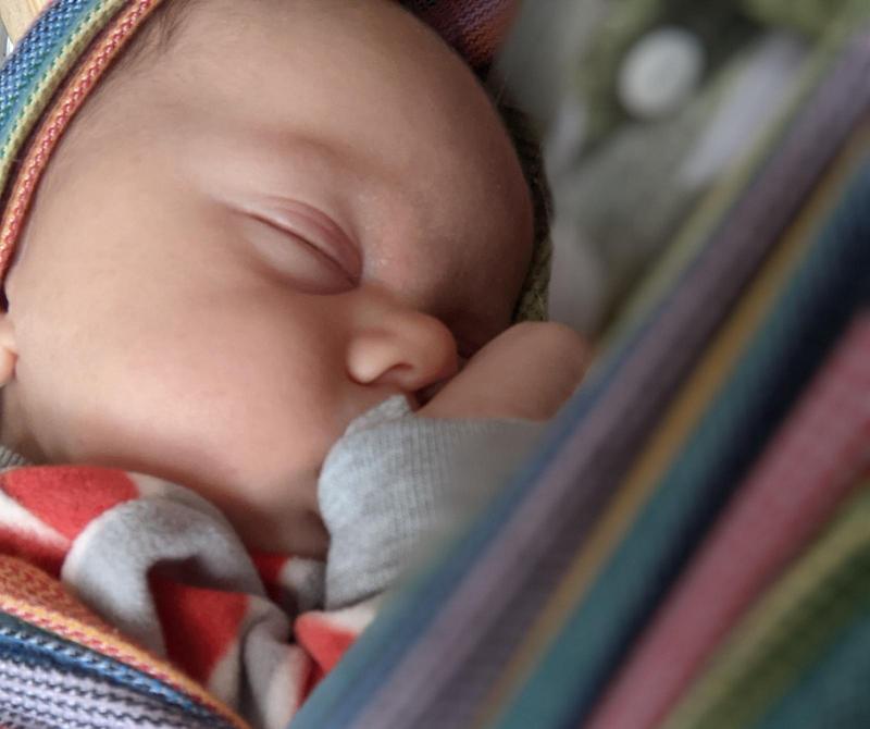 baby sleeping in a woven wrap on his mother