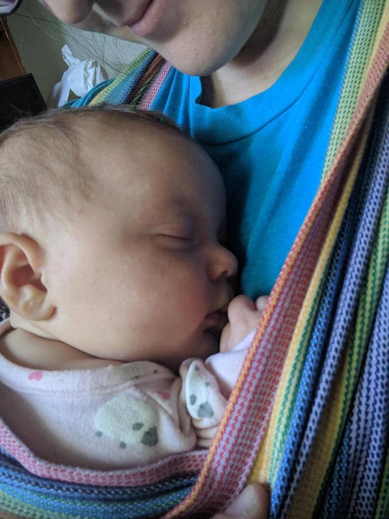 a baby happily asleep in a woven wrap carrier on mommy