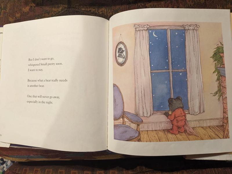 two-page spread from a picture book, with text on the left saying 'But I don't want to go, whispered Small  pretty soon. I want to stay. Because what a bear really needs is another bear. One that will never go away, especially in the night.' and an illustration on the right showing a young bear in pajamas standing sadly by a window, back to the viewer