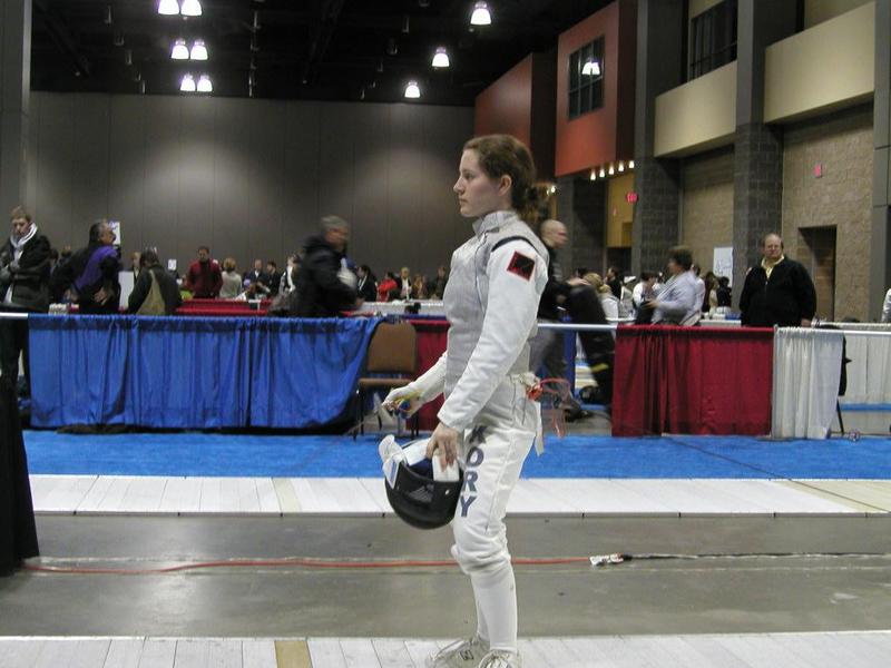 teenage jacqueline standing on a fencing strip, mask off, waiting for a bout