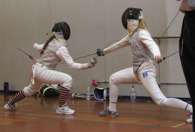 teenage jacqueline in fencing whites and stripy socks lunging at her opponent on strip