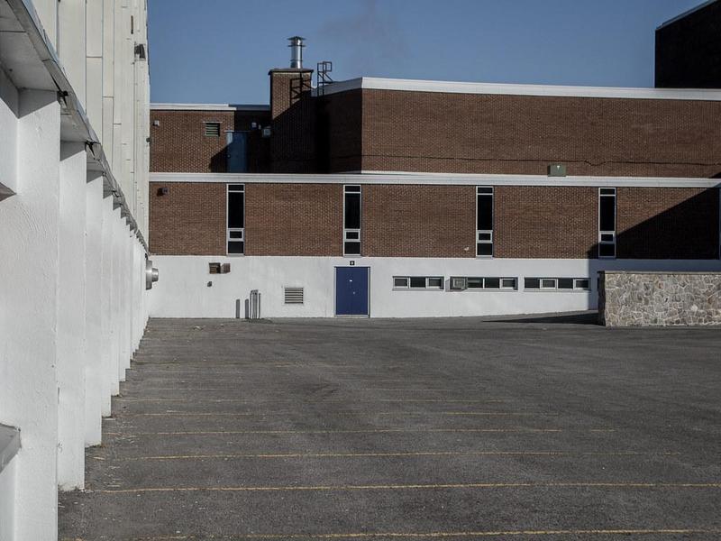 concrete and brick building with four narrow windows and a few long flat windows, surrounding a parking lot, looking a lot like a prison, nothing green or cheerful in sight