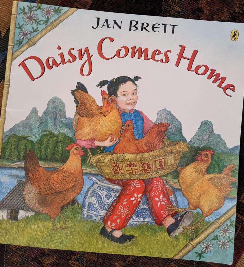 the cover of the picture book Daisy Comes Home by Jan Brett, featuring a young Chinese girl and some hens